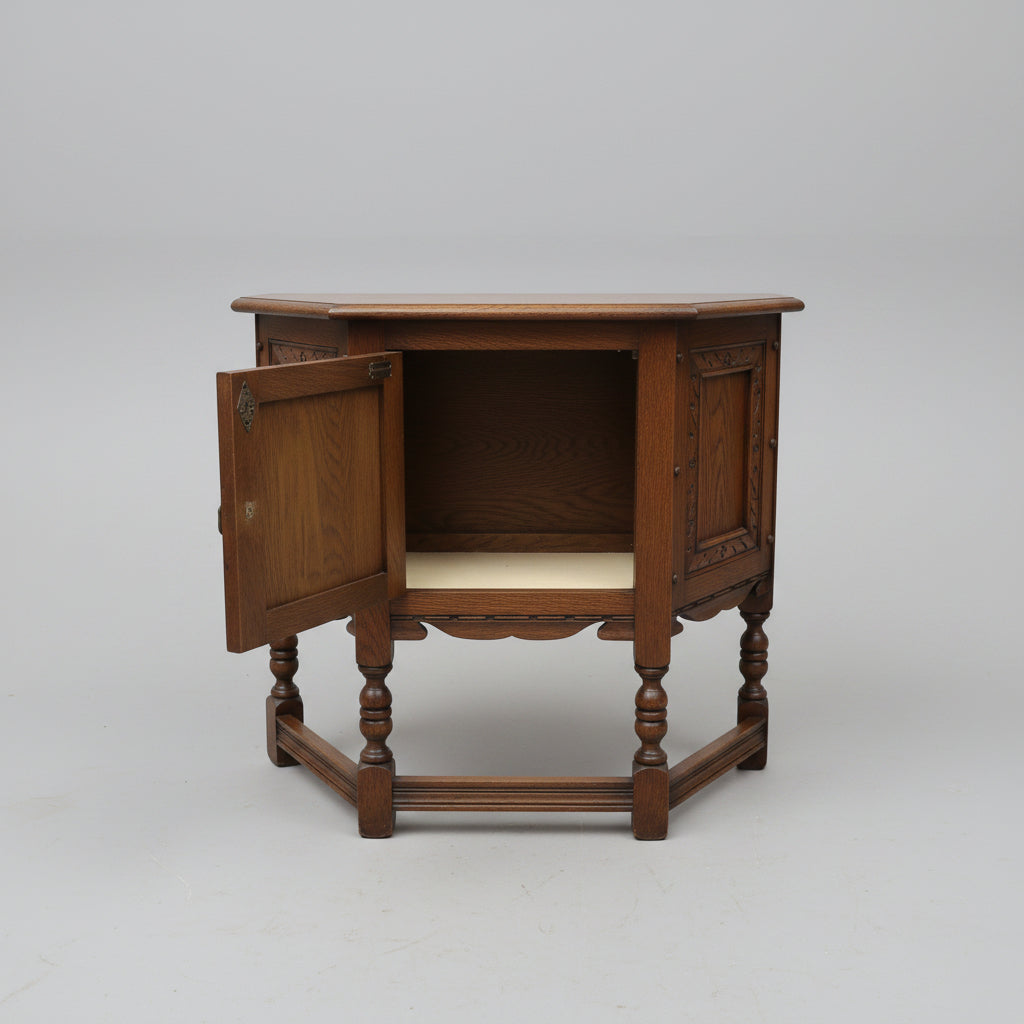 A dark brown wooden side table or cabinet with turned legs and an open door showing an interior shelf, photographed in a furniture store or warehouse setting.