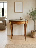 An elegant round console table with a chevron wood pattern, gold-toned legs, and a light stone top, styled in a warm, modern living room setting.