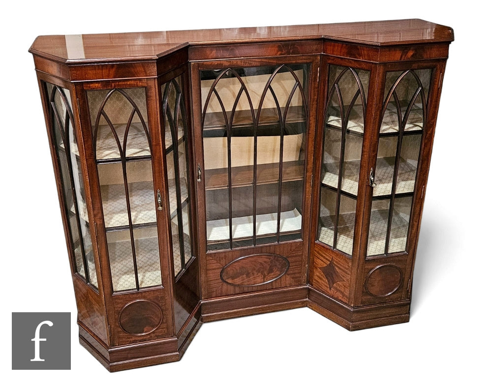 Edwardian inverted break front display cabinet of unusual form enclosed by lancet doors below a moulded edge top over a plinth base