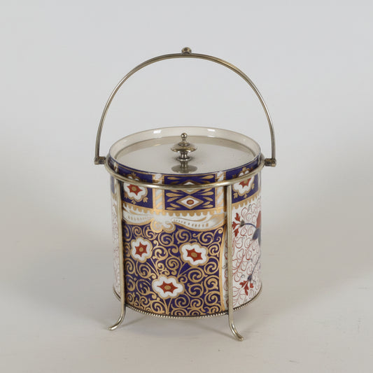 Two decorative metal and glass canisters with ornate silver-tone handles and lids, one featuring a white and blue floral pattern and the other a blue panel with white classical figures, set against a plain light background.