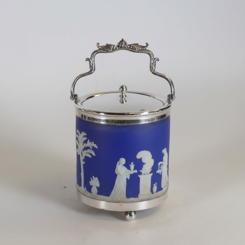 Two decorative metal and glass canisters with ornate silver-tone handles and lids, one featuring a white and blue floral pattern and the other a blue panel with white classical figures, set against a plain light background.