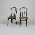 Two dark wood bentwood chairs with round seats, positioned on a worn concrete floor inside what appears to be a furniture showroom or warehouse.