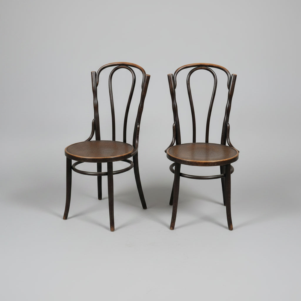 Two dark wood bentwood chairs with round seats, positioned on a worn concrete floor inside what appears to be a furniture showroom or warehouse.