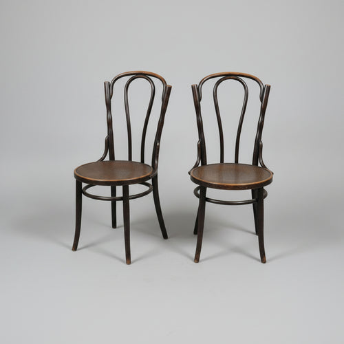 Two dark wood bentwood chairs with round seats, positioned on a worn concrete floor inside what appears to be a furniture showroom or warehouse.