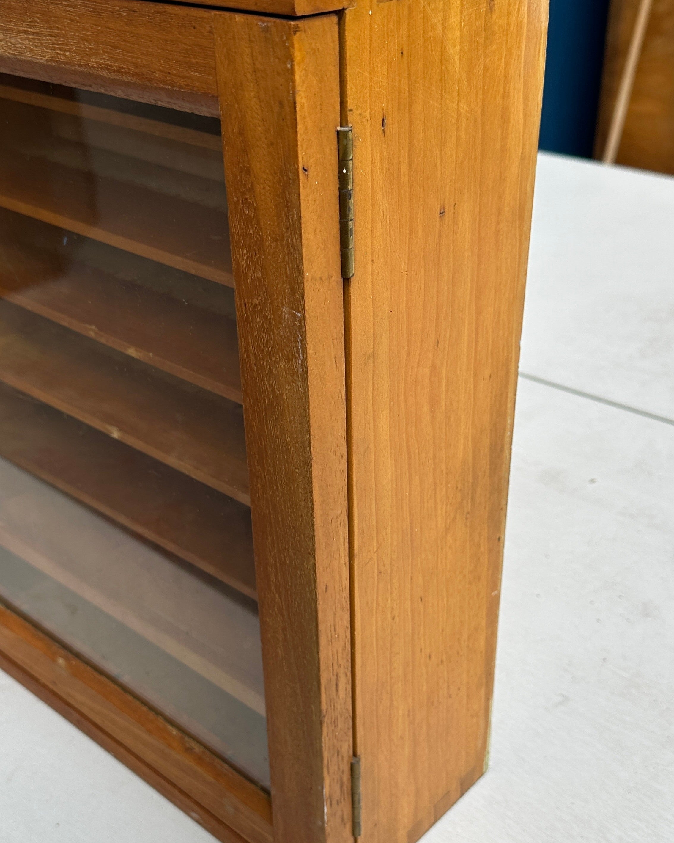 A vintage wooden display cabinet with a glass front door and internal shelves, shown on a white table.