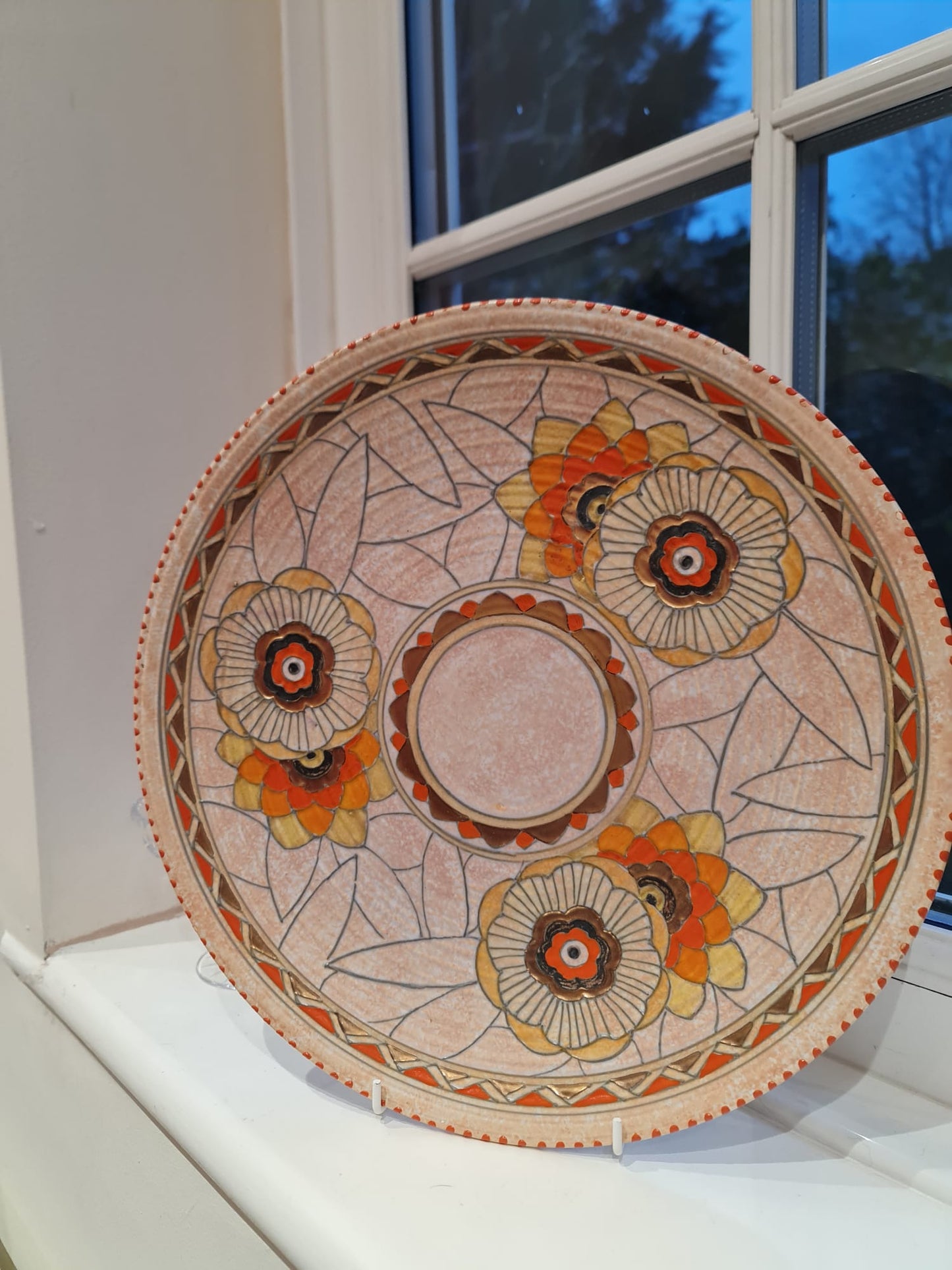 This collector plate, designed by Charlotte Rhead, features an intricate pattern of leaves and showcases the Art Deco style.
