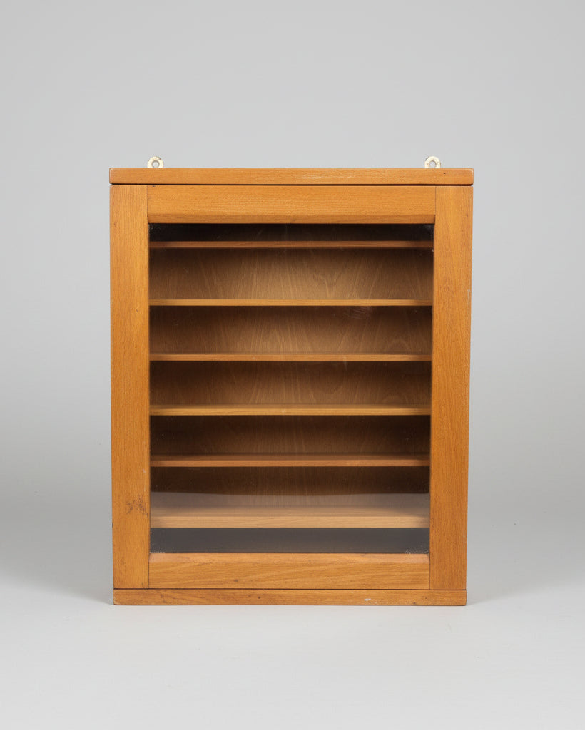 A vintage wooden display cabinet with a glass front door, showing multiple interior shelves, brass hanging hardware on the top, and a small white label with the number 232.