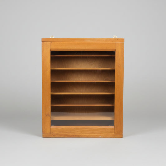 A vintage wooden display cabinet with a glass front door, showing multiple interior shelves, brass hanging hardware on the top, and a small white label with the number 232.