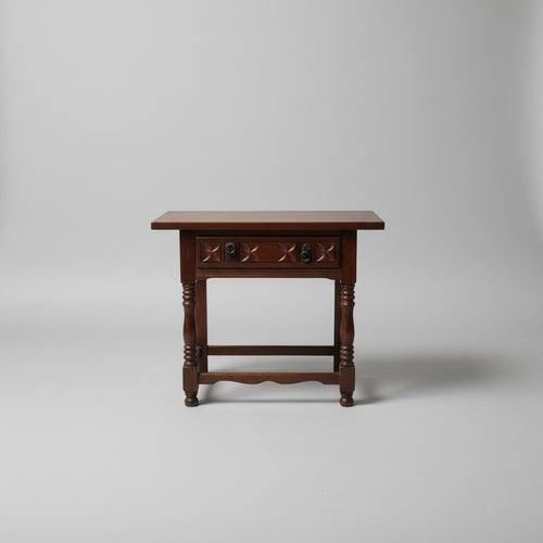 A 19th century oak wood table with a carved frieze drawer on turned supports, placed on a woven mat.