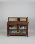 A dark wood china cabinet with glass doors in an antique shop, with a woman pointing at the cabinet top display.