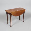 19th century oval mahogany drop-leaf table with tapered legs and pad feet, positioned on a concrete surface with a visible red paint marking.