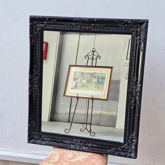 A VINTAGE BLACK WALL MIRROR WITH FOLIATE DECORATION