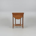 A dark brown wooden dressing table with a drop-leaf top, twisted legs, a shelf, and an attached storage chest, photographed in a furniture showroom.