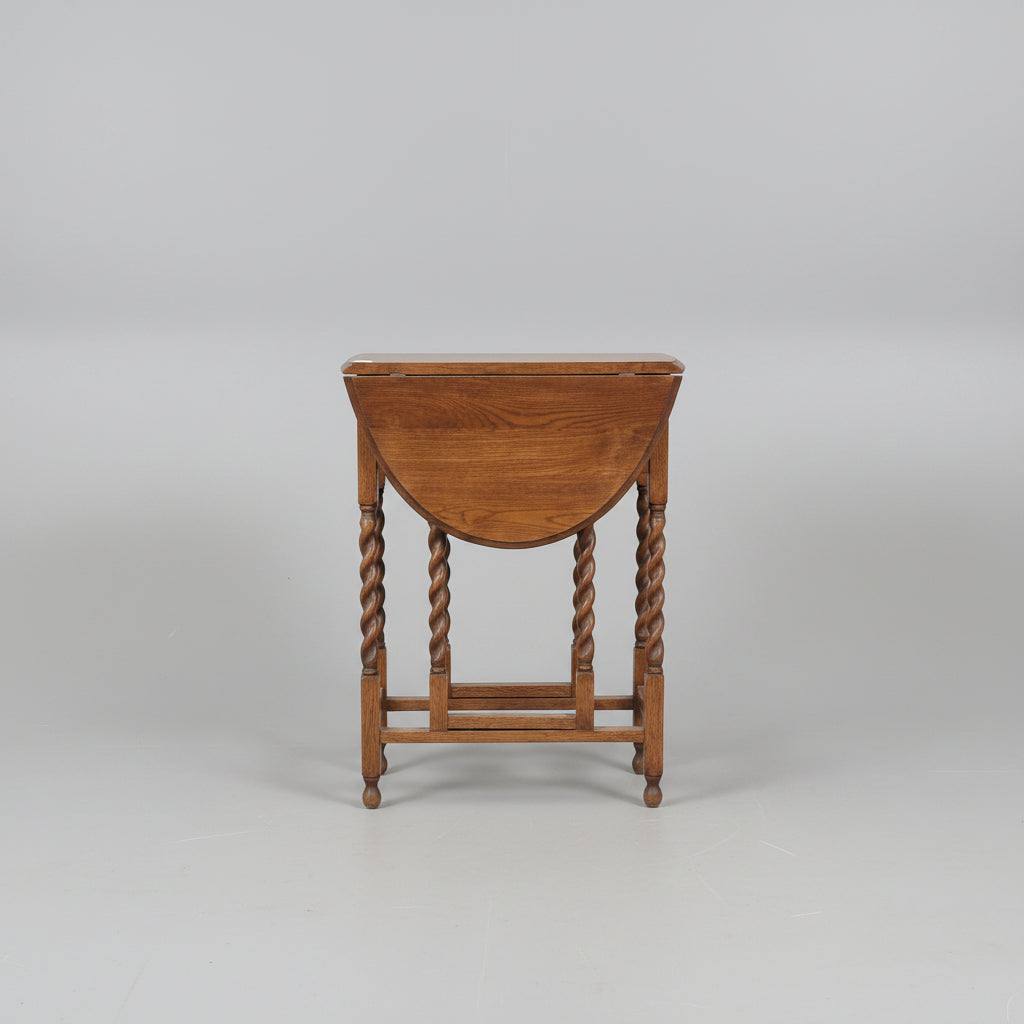 A dark brown wooden dressing table with a drop-leaf top, twisted legs, a shelf, and an attached storage chest, photographed in a furniture showroom.