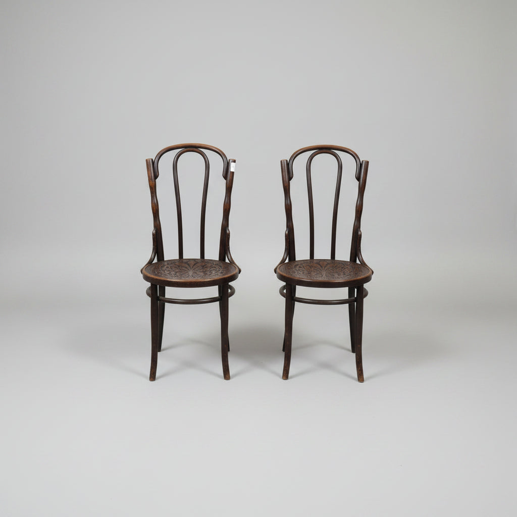 Two dark brown bentwood dining chairs with woven cane seats, positioned side-by-side on a concrete floor in what appears to be a furniture showroom or warehouse.