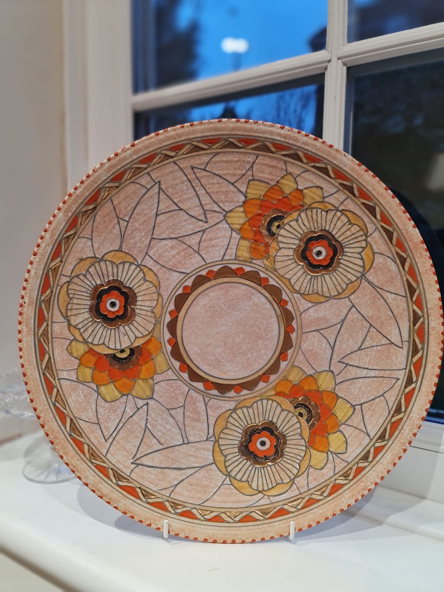 This collector plate, designed by Charlotte Rhead, features an intricate pattern of leaves and showcases the Art Deco style.