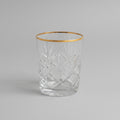 A clear cut-crystal tumbler glass with a diamond pattern, sitting on a brown leather surface in a softly blurred indoor setting.