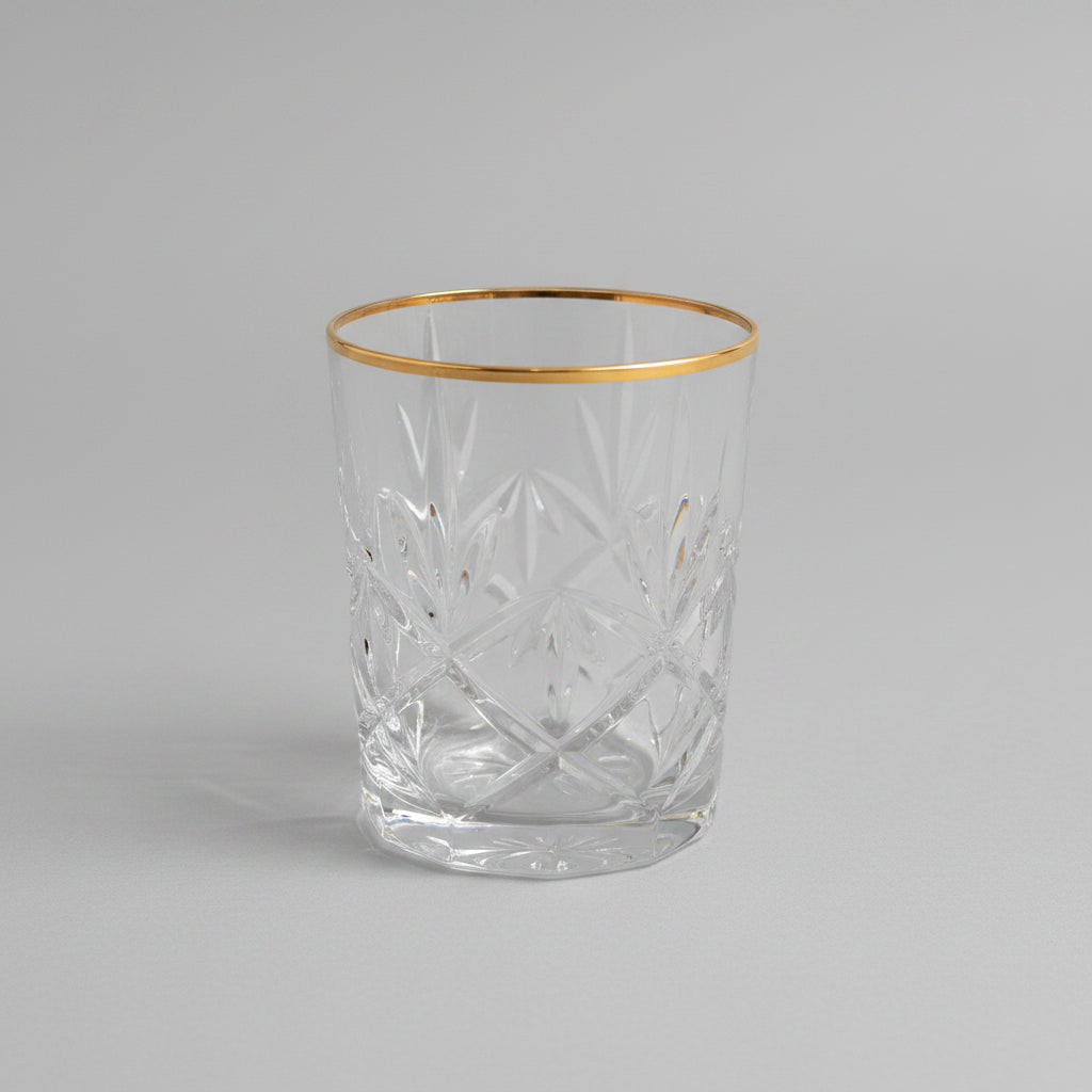 A clear cut-crystal tumbler glass with a diamond pattern, sitting on a brown leather surface in a softly blurred indoor setting.