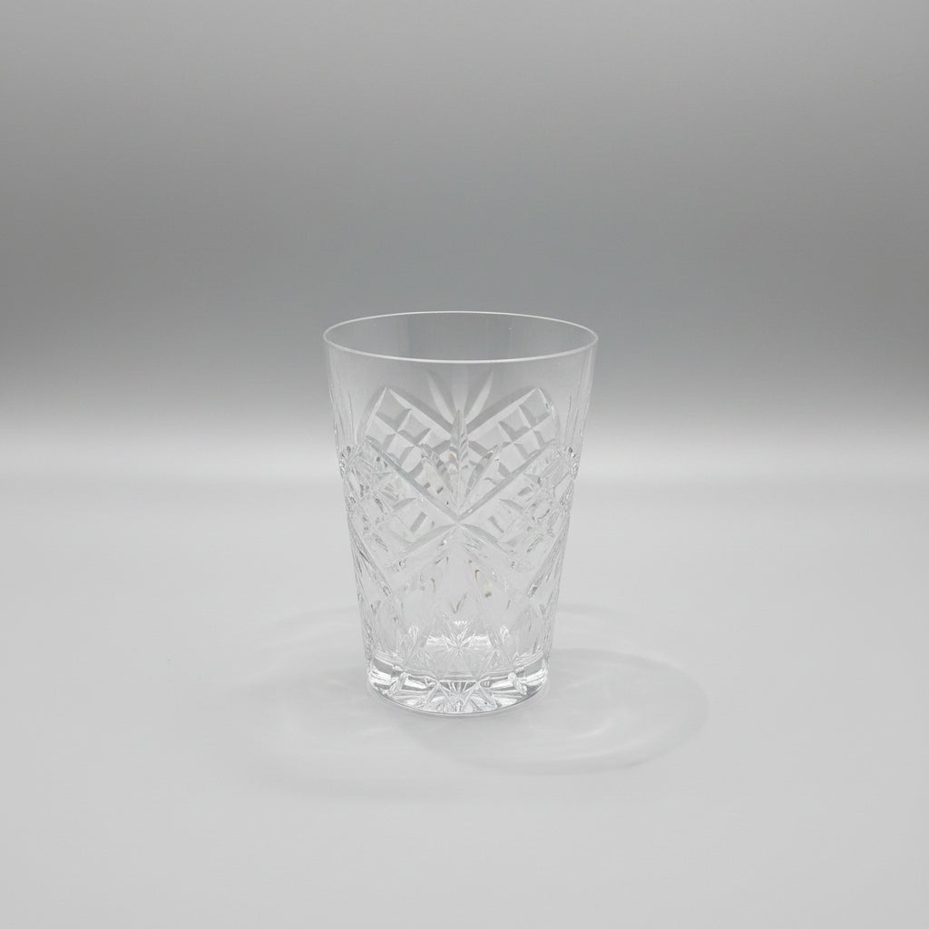 A clear cut-crystal tumbler with geometric starburst patterns, resting on a dark brown wooden table.