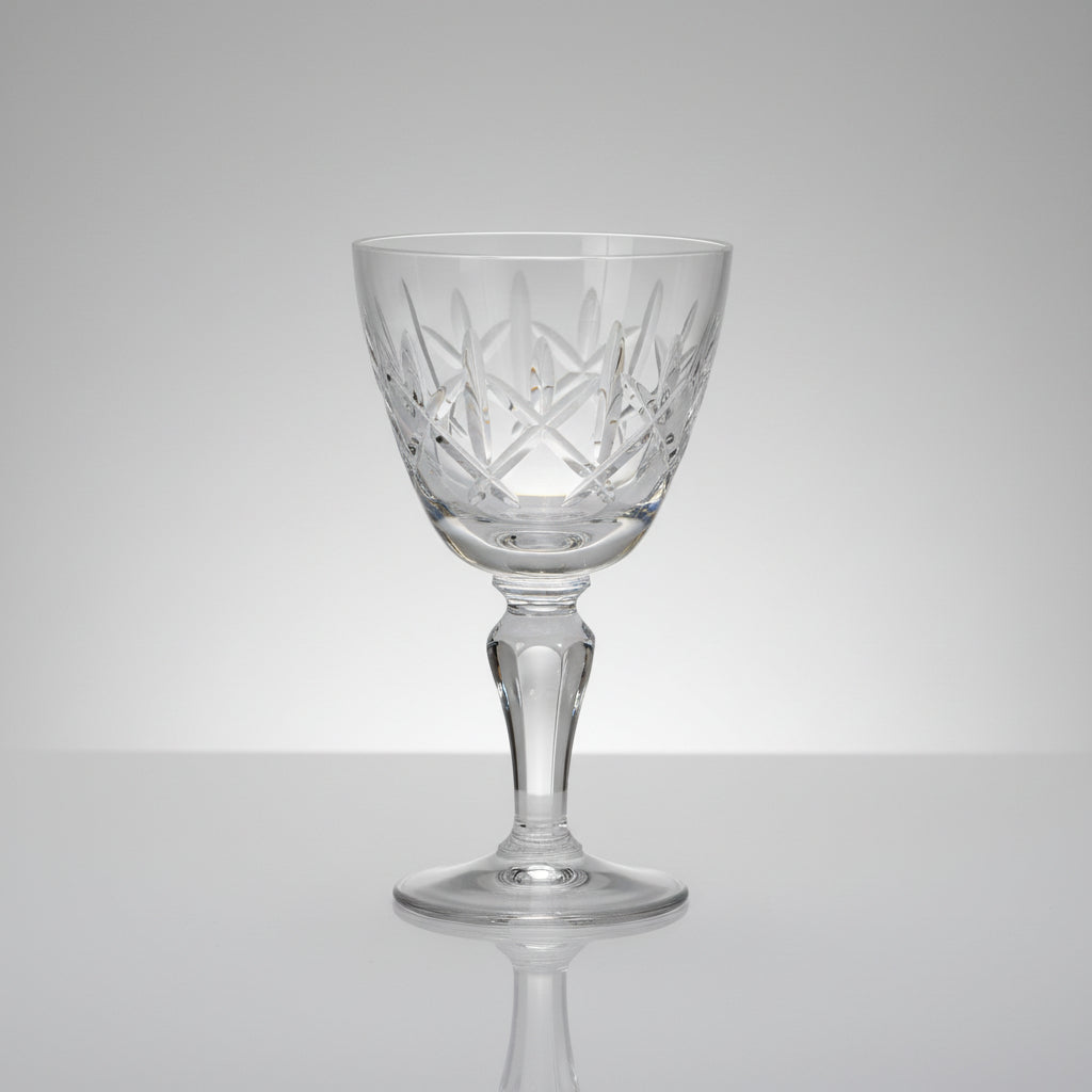 A clear cut-crystal wine glass with a diamond pattern, set on a dark brown wooden table.