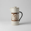 Coffee cup with a brown spiral design on a white surface near a window.
