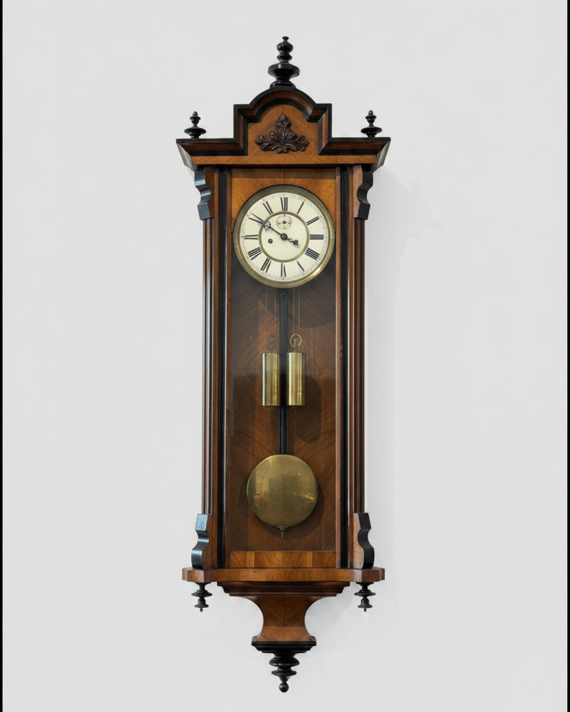 A traditional wall-mounted grandfather clock with a wooden case and a white clock face, standing above a shelf with a plant and some decorative items.
