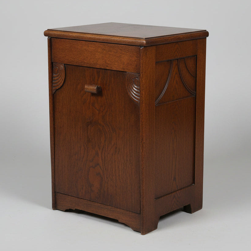 A vintage dark brown wooden chest or cabinet with a single front drawer and a small round knob, photographed in a room with a worn multicolored floor and other furniture partially visible.