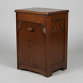 A vintage dark brown wooden chest or cabinet with a single front drawer and a small round knob, photographed in a room with a worn multicolored floor and other furniture partially visible.