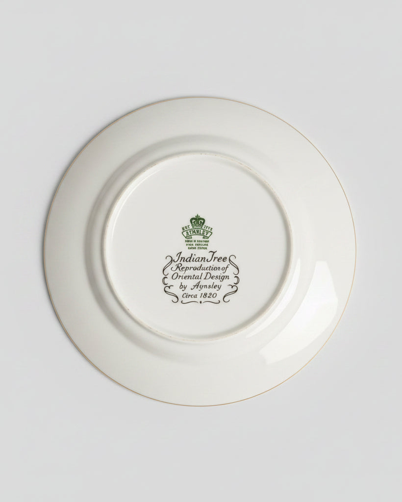 A white ceramic plate shown from the back, featuring a green printed crest and the text 'Medicine Tree Apothecary Design by Audrey Cline 1820'. The plate is placed on a dark brown leather surface with gold decorative borders.