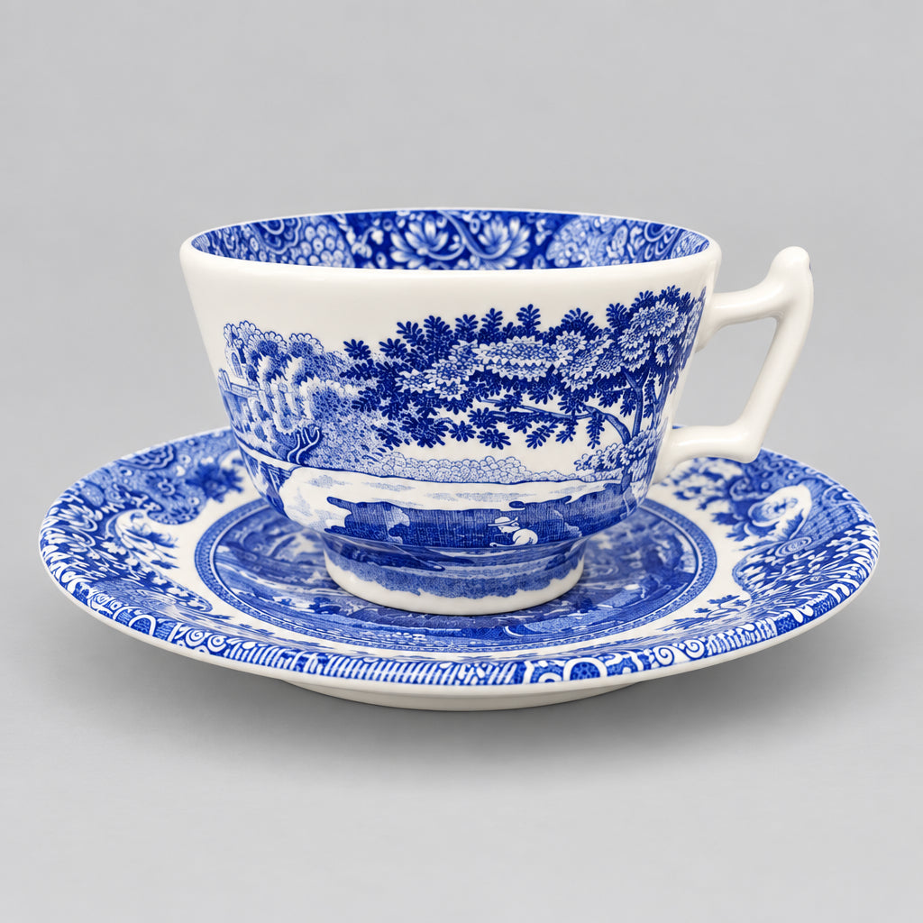 A classic blue and white porcelain teacup and saucer set with a detailed landscape print, displayed on a wooden table against a light wall.
