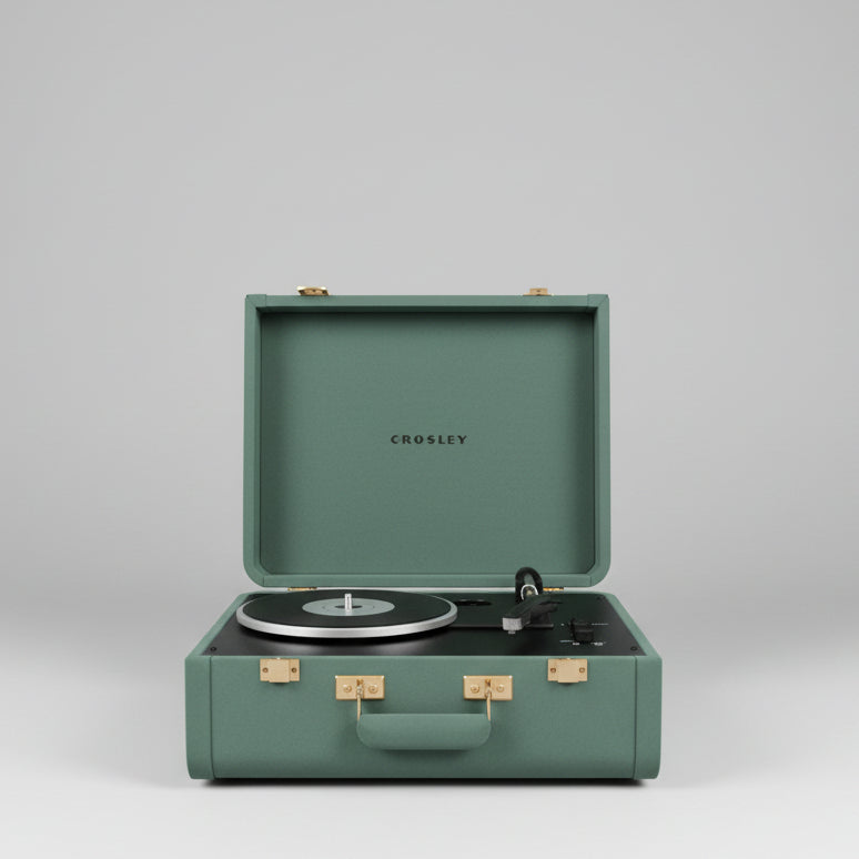 A Crosley portable record player in a teal-green hard case, shown open with a vinyl record on the turntable in a shop setting.