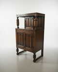 An antique dark wood hutch or cabinet with carved panel doors, turned legs, and a glass-front side cabinet, photographed in a furniture showroom.