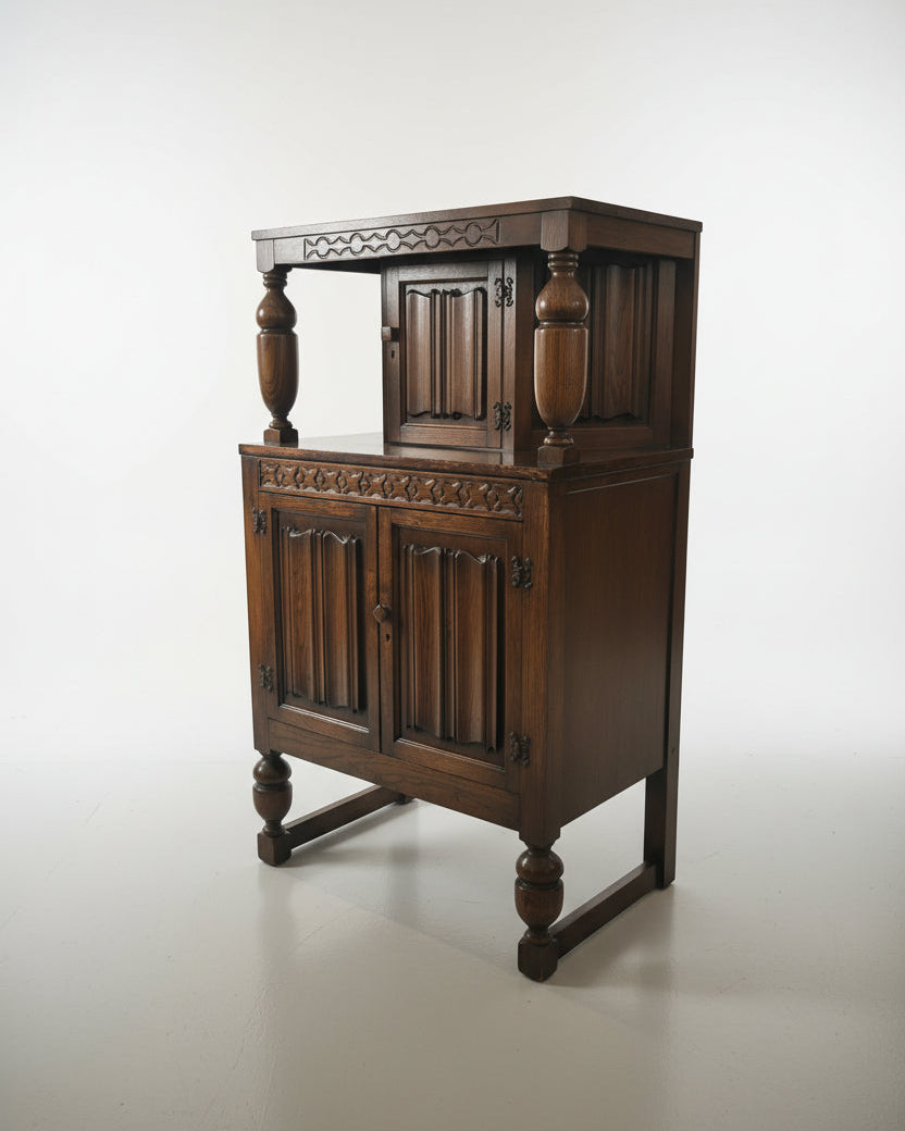 An antique dark wood hutch or cabinet with carved panel doors, turned legs, and a glass-front side cabinet, photographed in a furniture showroom.
