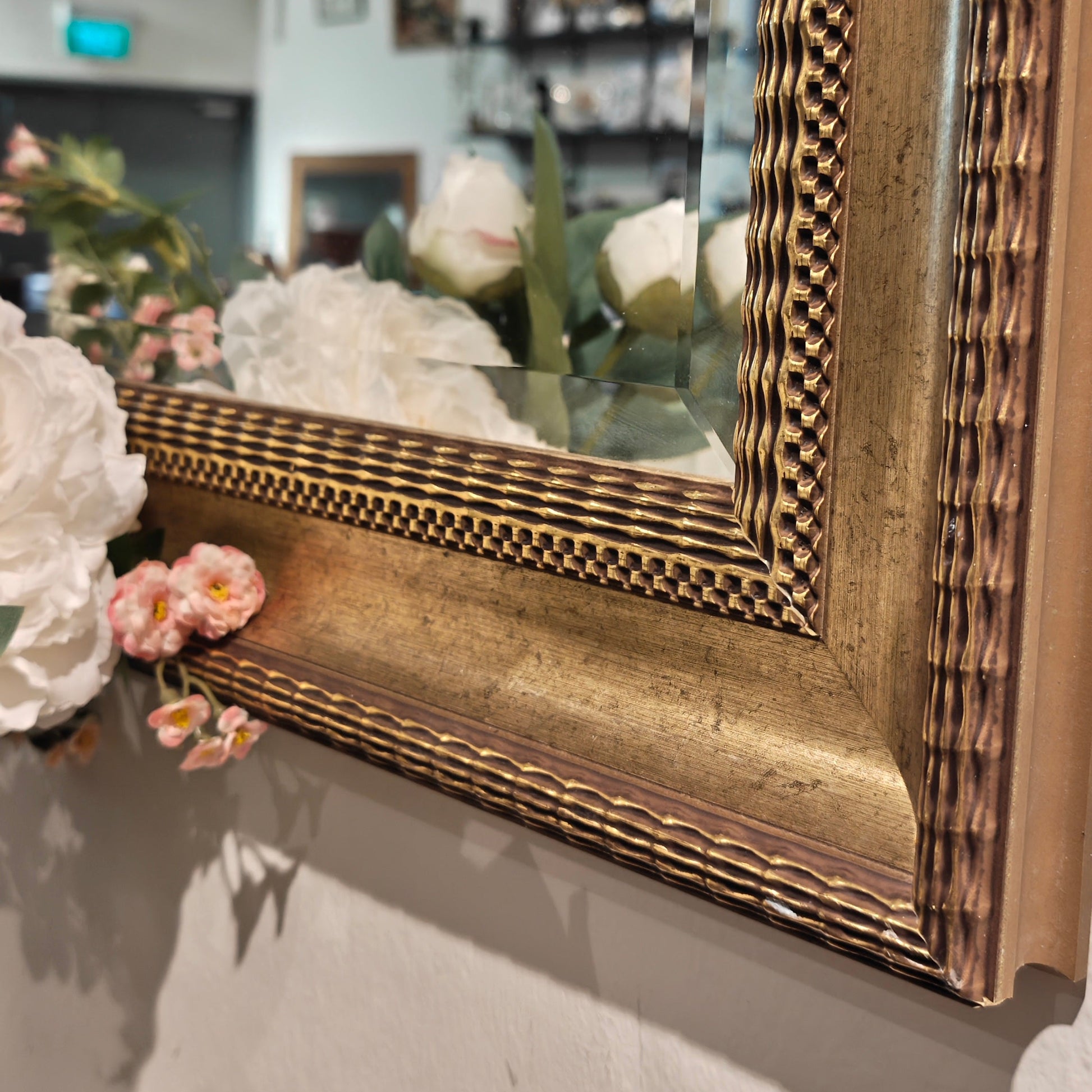 Decorative gold-framed mirror on a wall with floral arrangements.