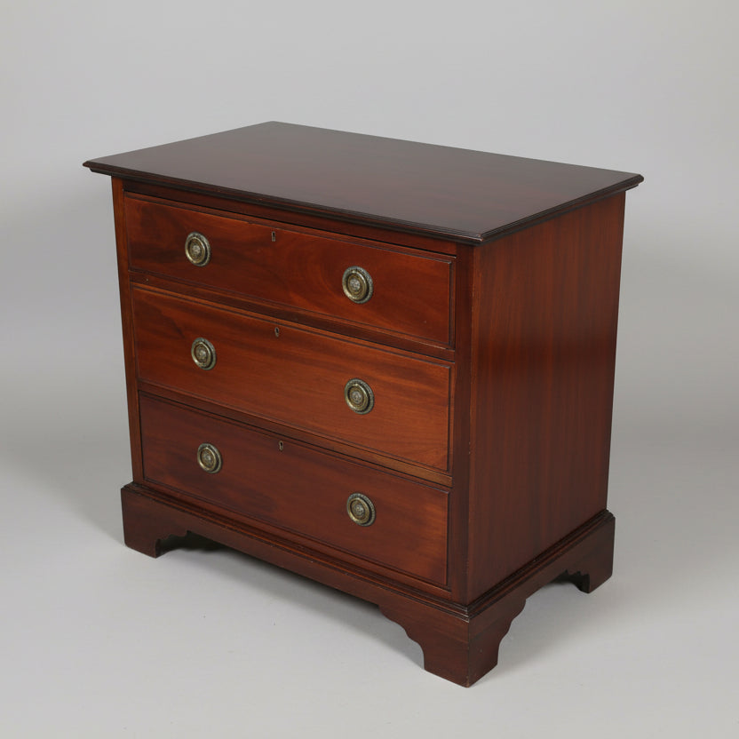 An early 19th century small mahogany chest of drawers with oak lining and original handles, displayed on a shaped apron.