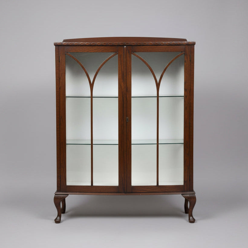 A dark brown wooden display cabinet with glass doors featuring a Gothic arch design, shown in what appears to be a warehouse or furniture showroom.