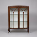 A dark brown wooden display cabinet with glass doors featuring a Gothic arch design, shown in what appears to be a warehouse or furniture showroom.