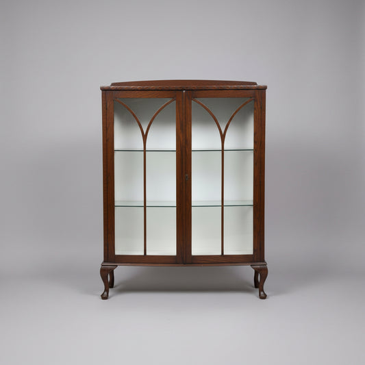 A dark brown wooden display cabinet with glass doors featuring a Gothic arch design, shown in what appears to be a warehouse or furniture showroom.