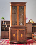 Wooden display cabinet with glass doors in a room setting.
