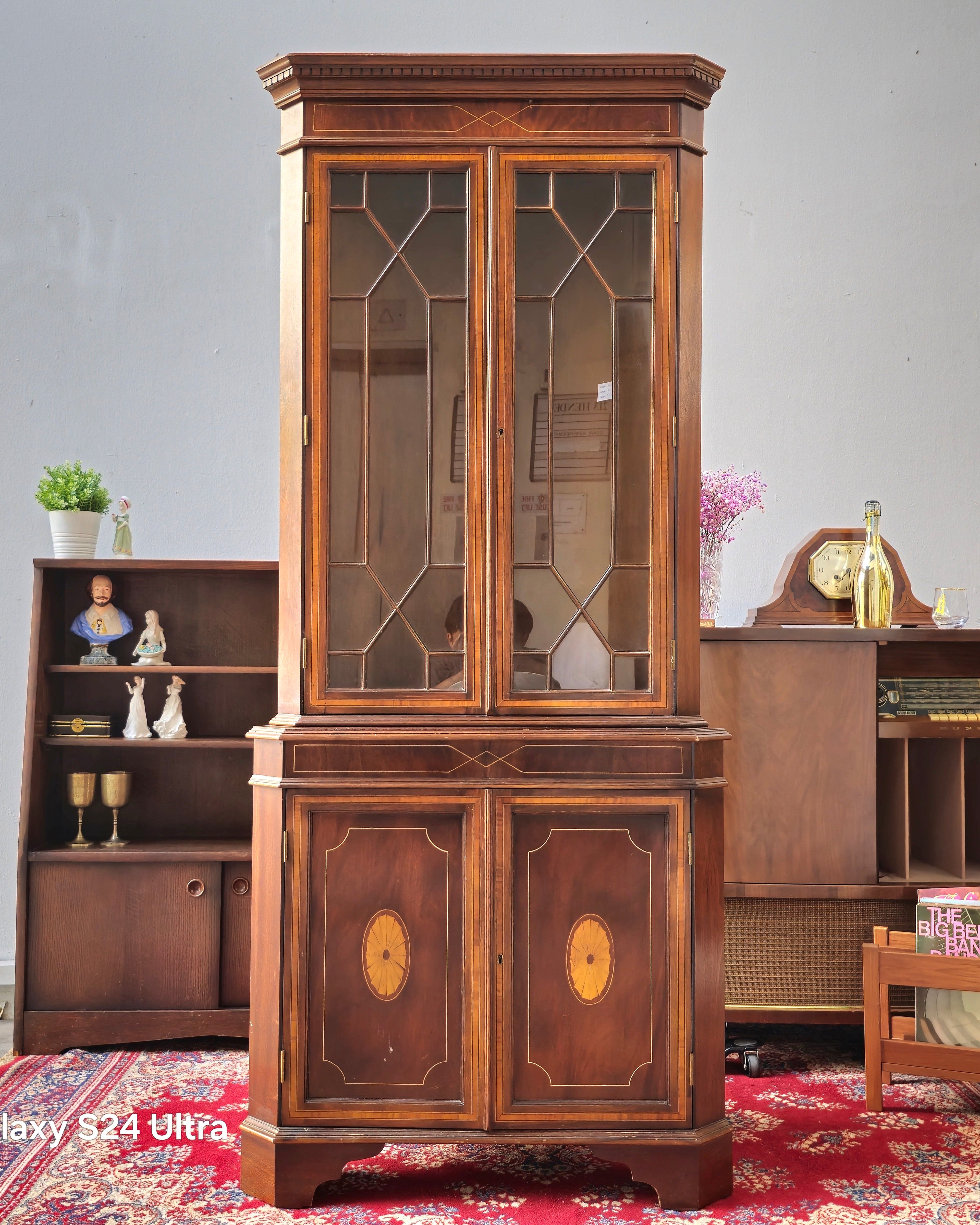 Wooden display cabinet with glass doors in a room setting.
