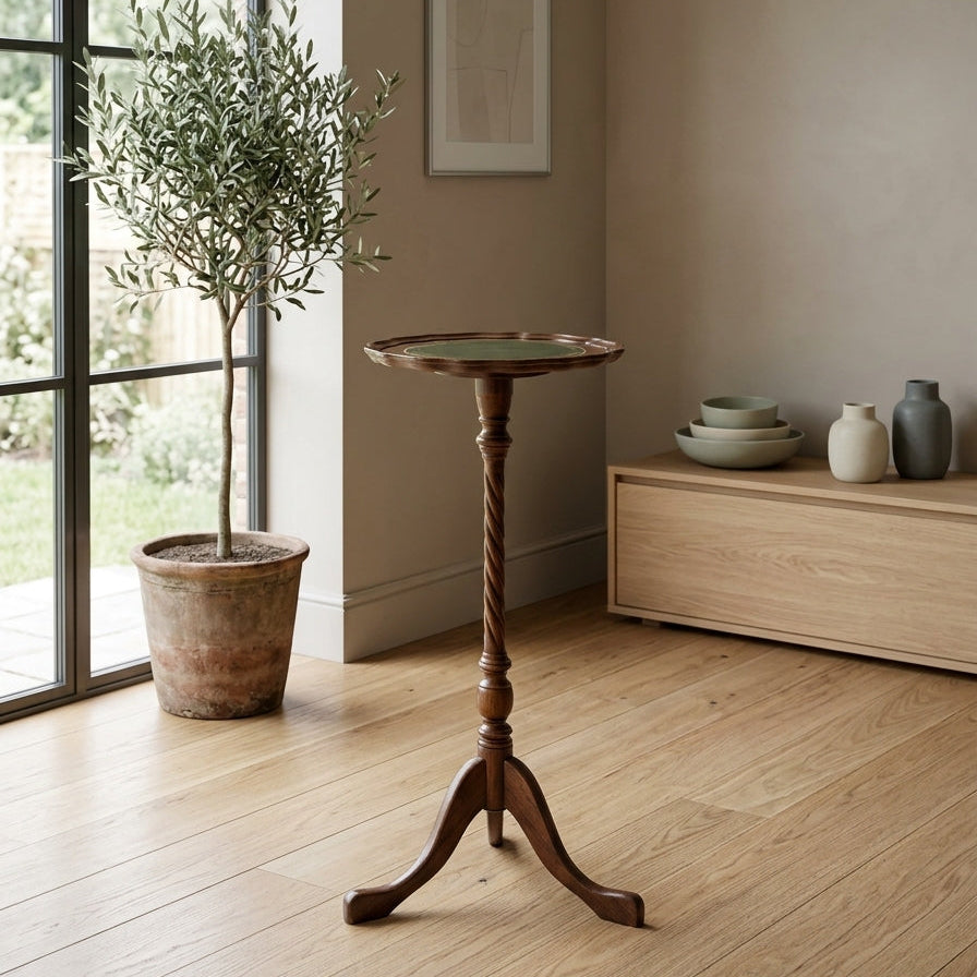 A small round wooden side table with a twisted pedestal base and three curved legs, styled in a bright, modern room with a potted olive tree and a light wood cabinet.