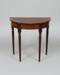A vintage wooden half-round console table with a dark brown leather inlay and gold decorative border, shown in a cluttered storage or warehouse setting.