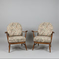 Two vintage wooden armchairs with patterned beige and brown upholstery, shown in a warehouse or showroom setting with a red door and red floor.