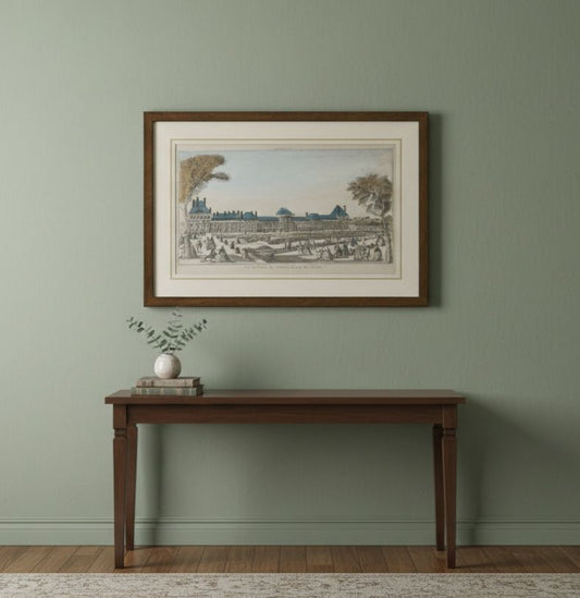 Framed artwork on a wall above a wooden table with a plant and books.