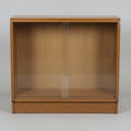 A mid-century wooden display cabinet with two glass sliding doors, shown in what appears to be a furniture showroom or warehouse.