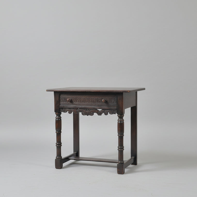 Wooden side table with decorative items on a red patterned rug against a white wall.