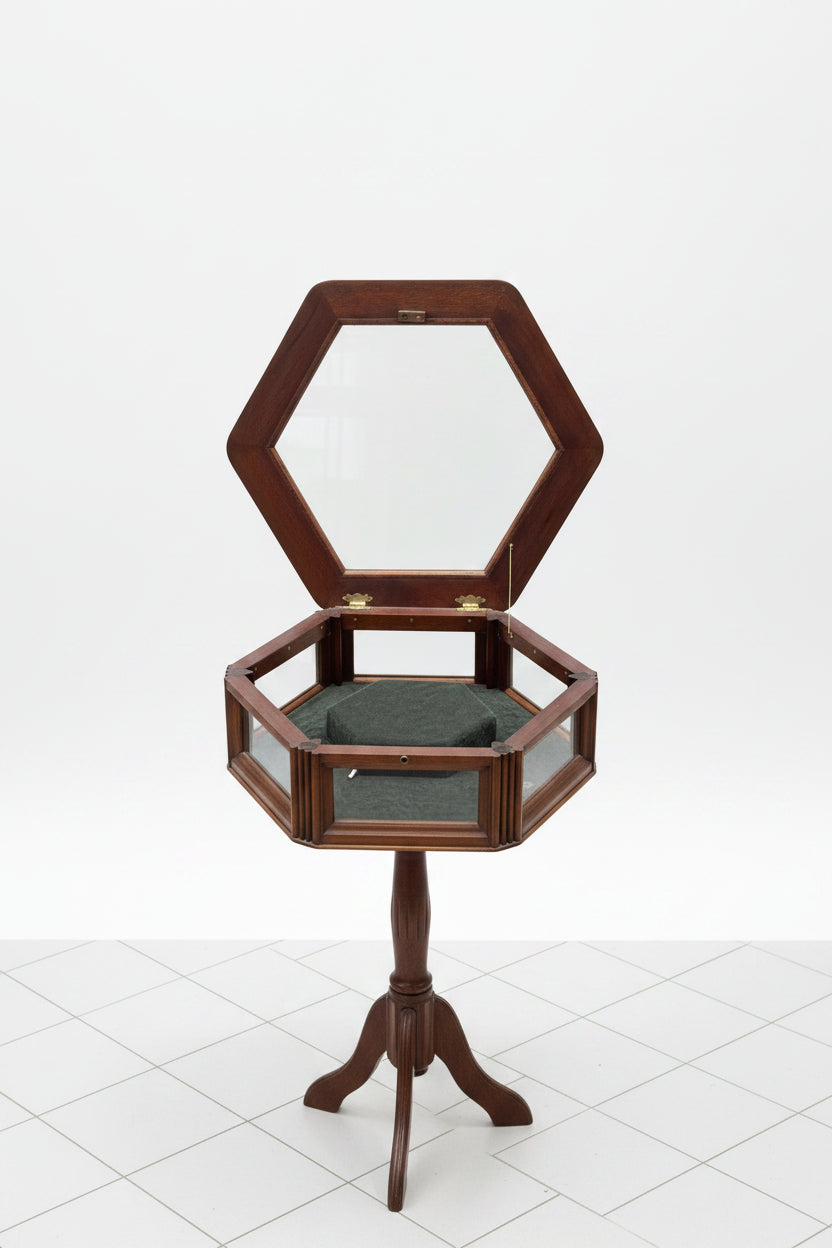 A hexagonal wooden display case with an open top mirror, featuring a dark green velvet interior and a three-legged stand, set on a gray wood-look floor against a white wall.