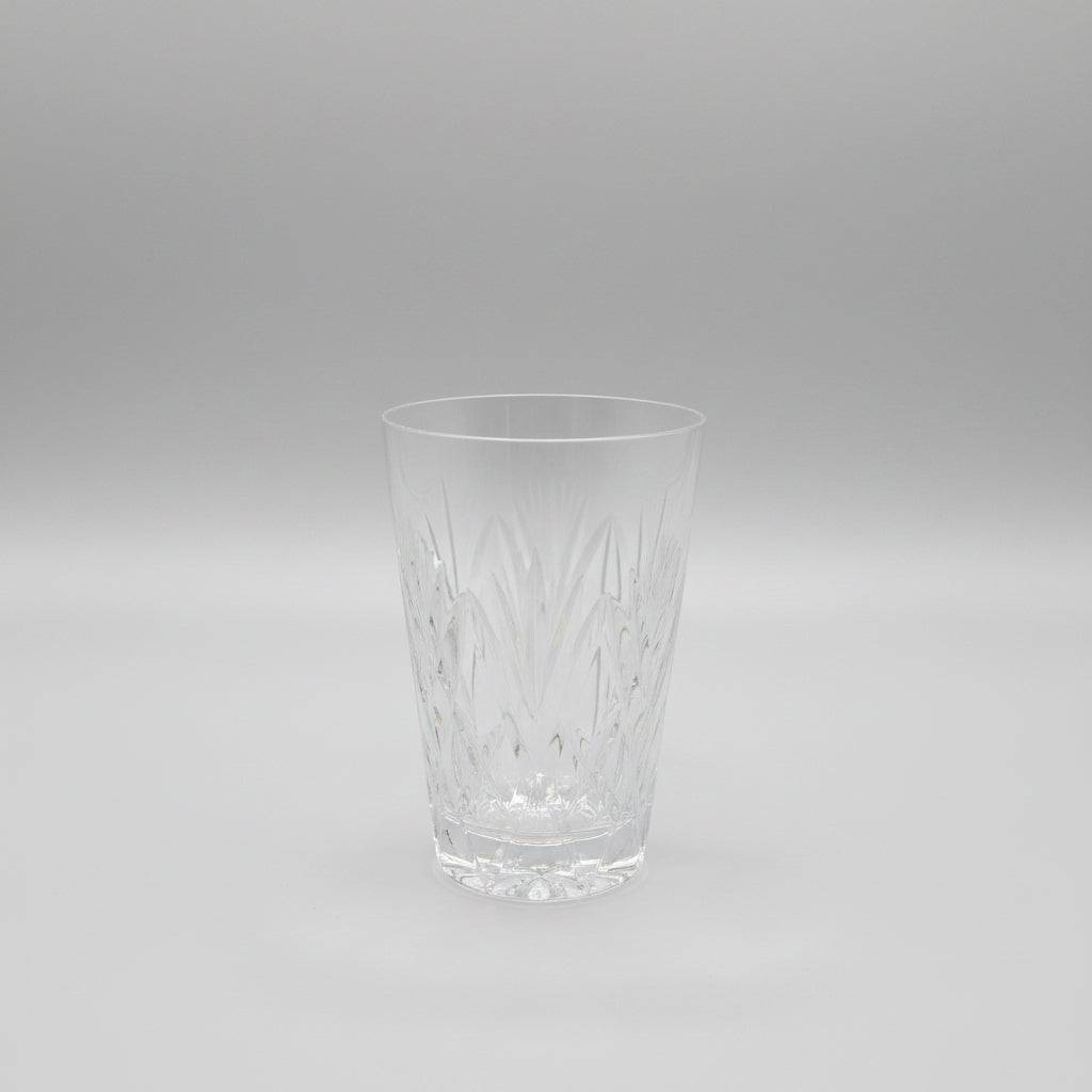 A clear cut-crystal style tumbler glass with a faceted geometric pattern, sitting on a dark brown wooden table.