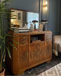 Wooden sideboard with decorative items in a room with a plant and chair.