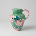 Decorative ceramic pitcher with apple design on a lace tablecloth